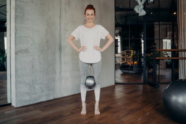 Sportive redhead woman holding mini pilates ball with her knees